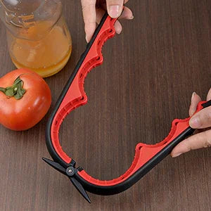 Jar opener tool with ergonomic red grip held over a table near a tomato and drink bottle