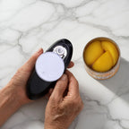 Hands using an electric can opener next to an open can of peaches on a marble countertop