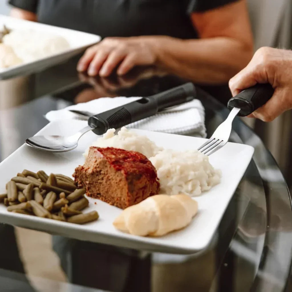 Adaptive utensils with large grips used to eat mashed potatoes, green beans, and meatloaf