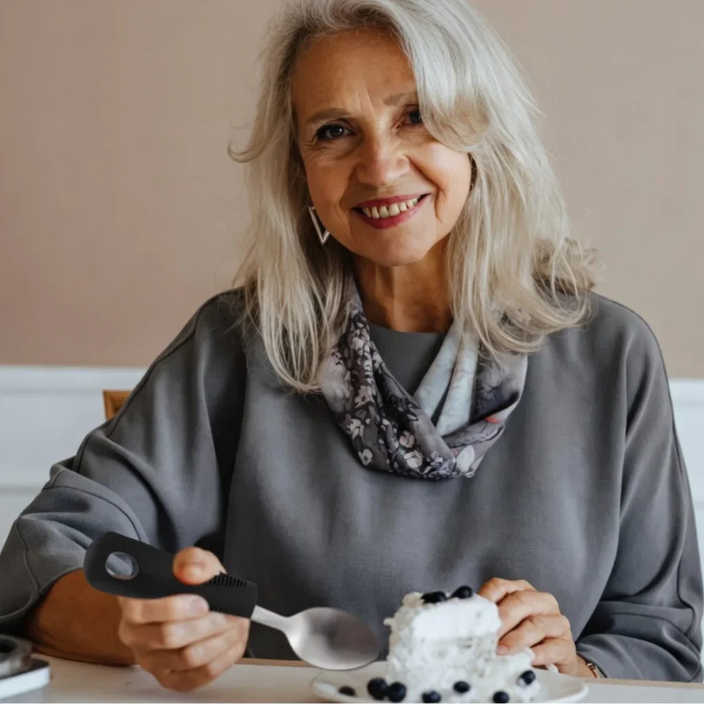 Older woman using ergonomic utensil to eat cake, adaptive aid for limited mobility
