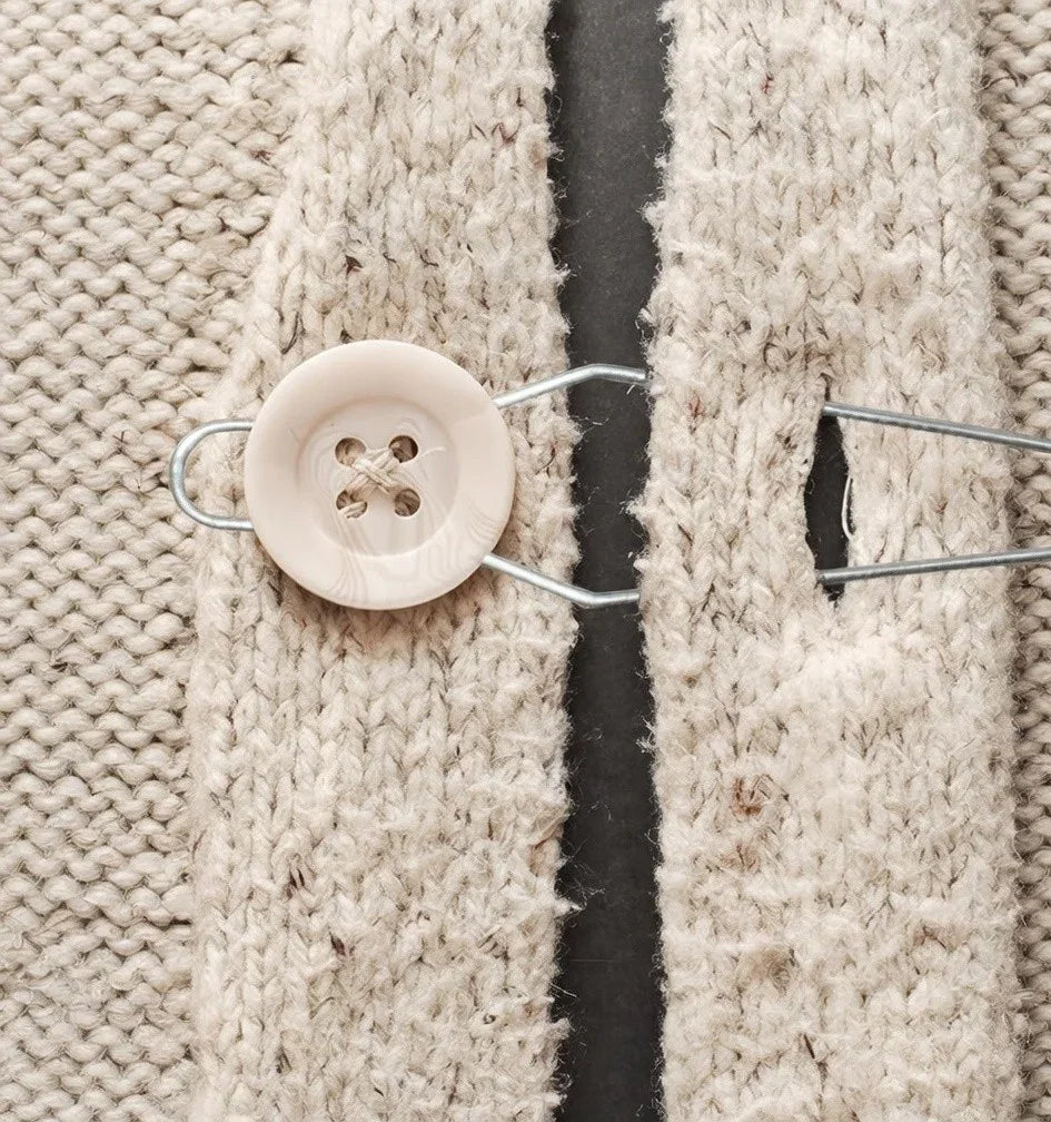 Button hook tool fastening a button on a chunky knit cardigan for easy dressing