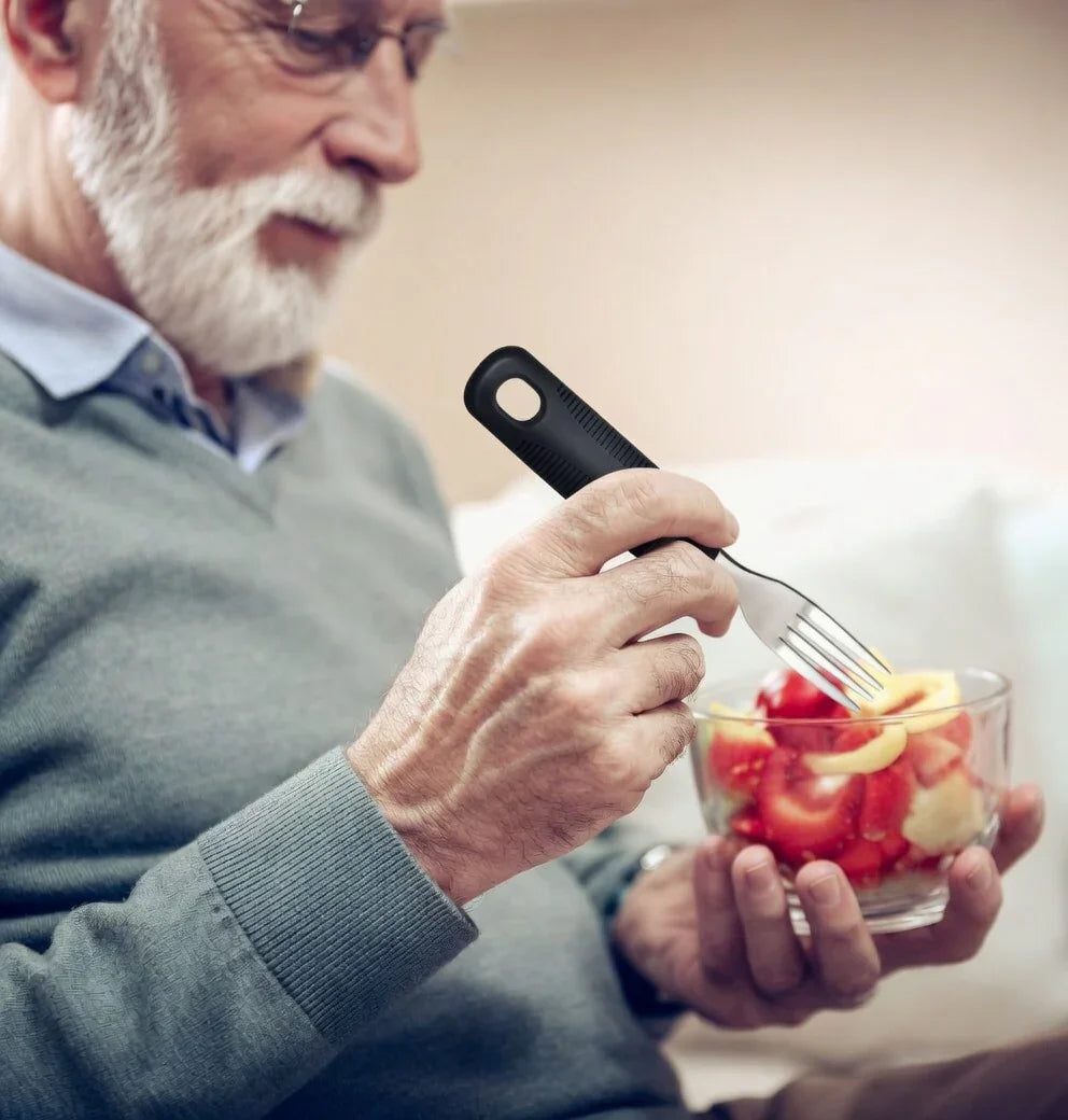 Elderly man eating fruit salad with an ergonomic fork for arthritis or limited mobility.