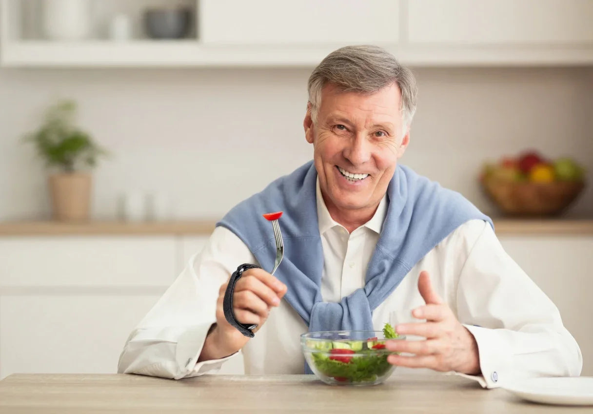 Smiling man using adaptive utensil aid to eat salad in bright kitchen