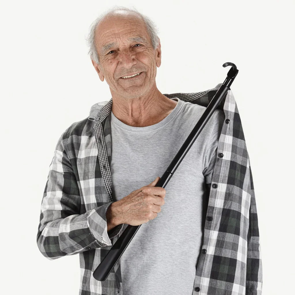 Older man using black adaptive dressing aid stick to put on plaid shirt